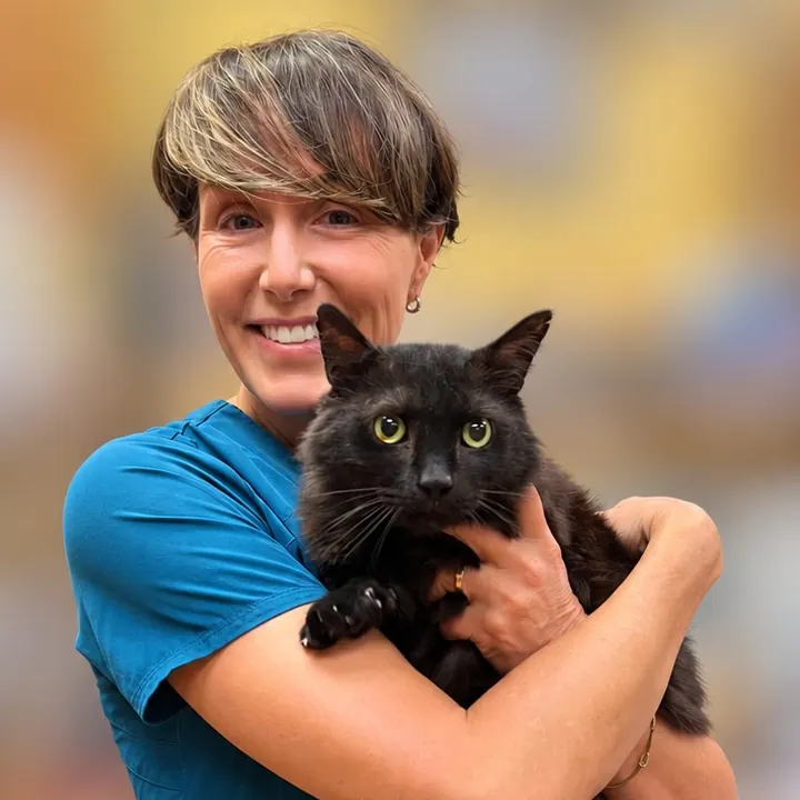 Dr. Chrysa Dunser in teal scrubs smiling and holding a black cat