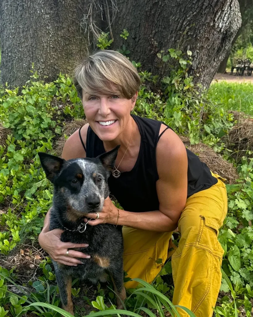 Dr. Chrysa Dunser kneeling beside her blue heeler under an oak tree