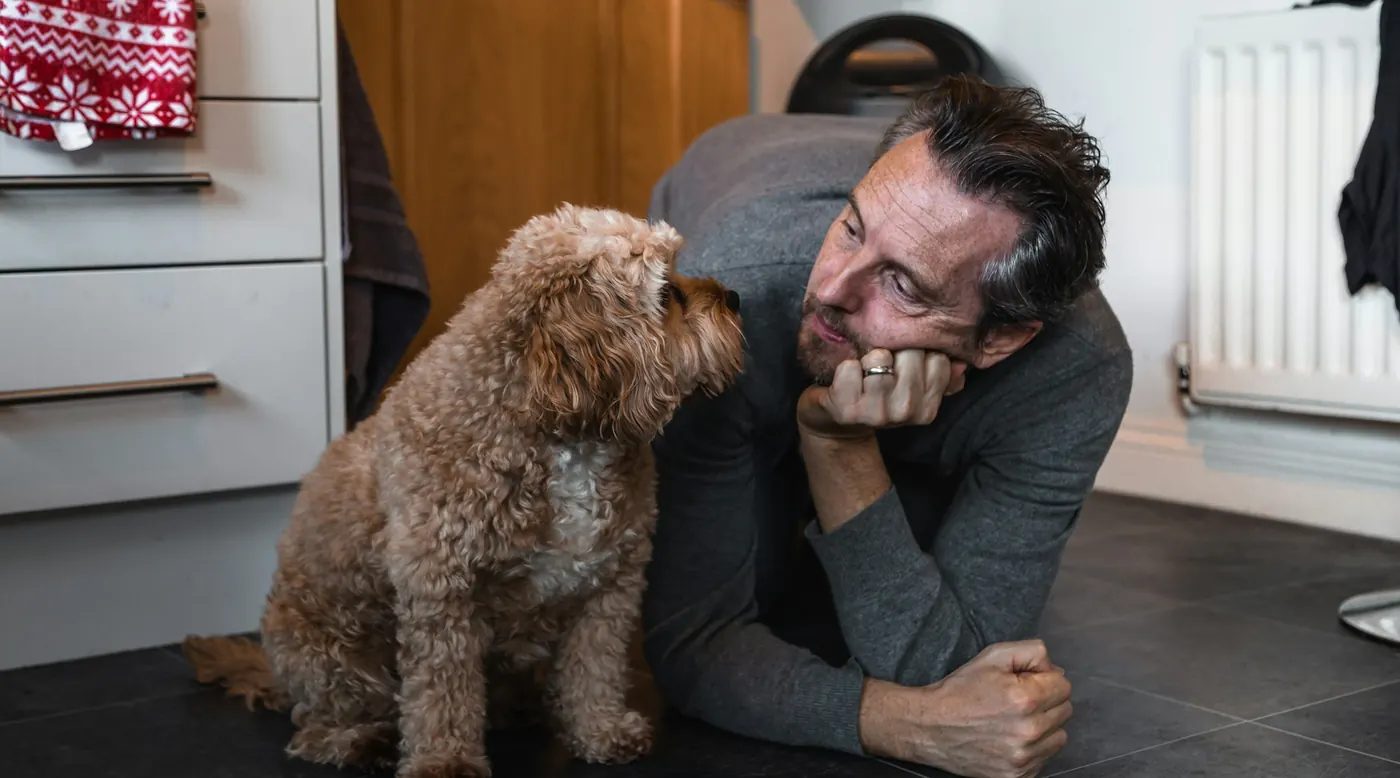 Man lying on the kitchen floor at eye level with his curly-coated dog