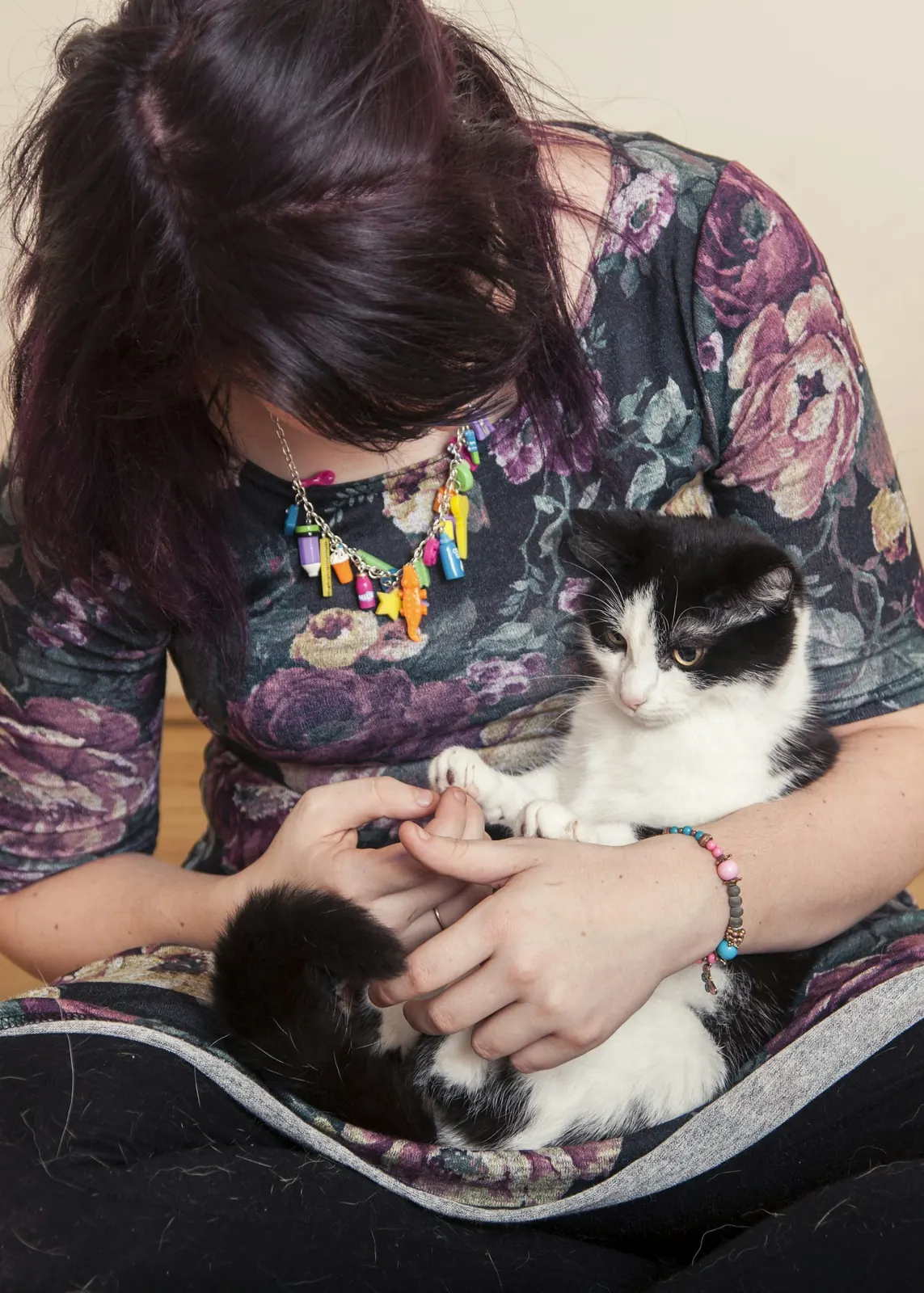 Woman in a floral top cuddling a black and white cat on her lap