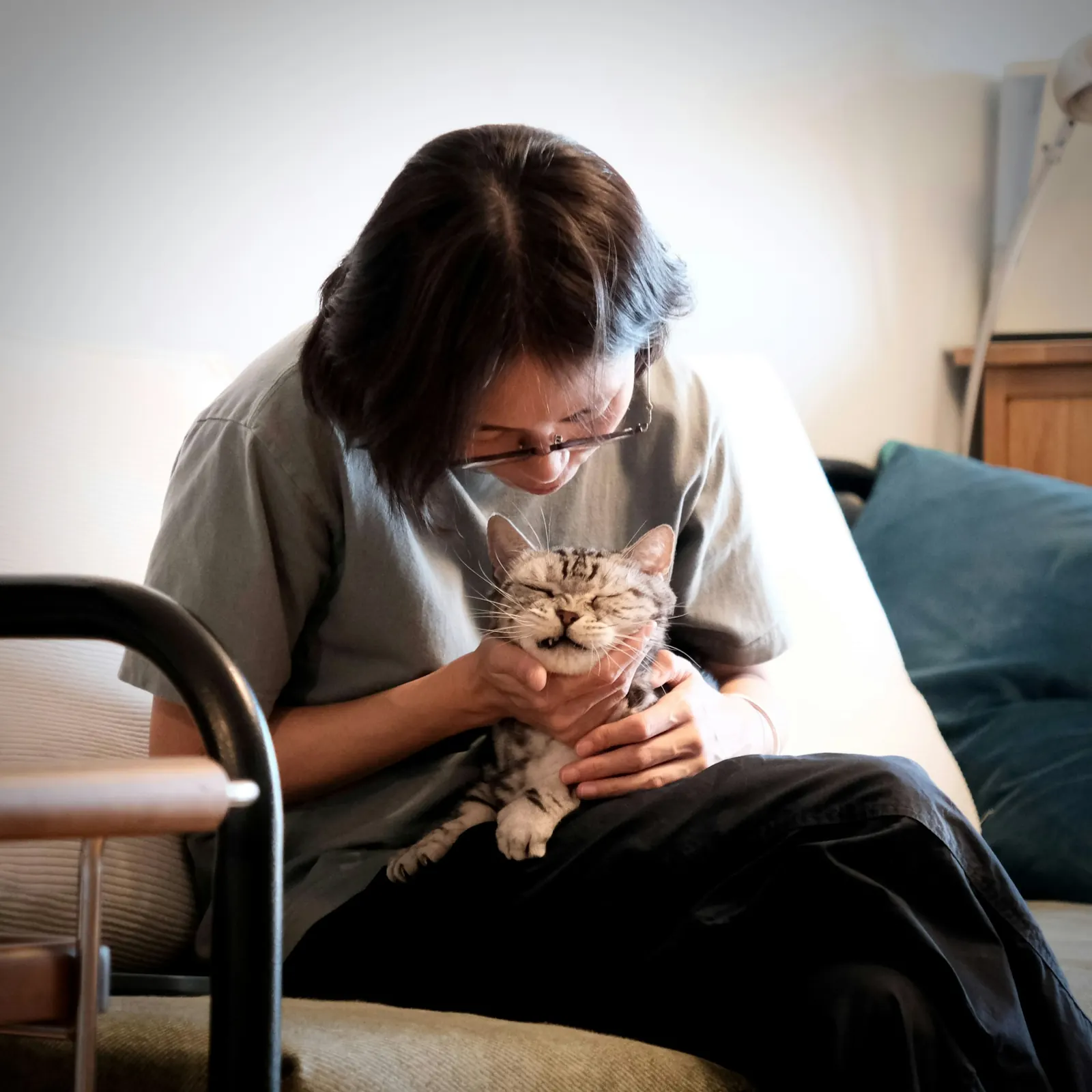 Woman in a grey t-shirt calmly cuddling a tabby cat on her lap