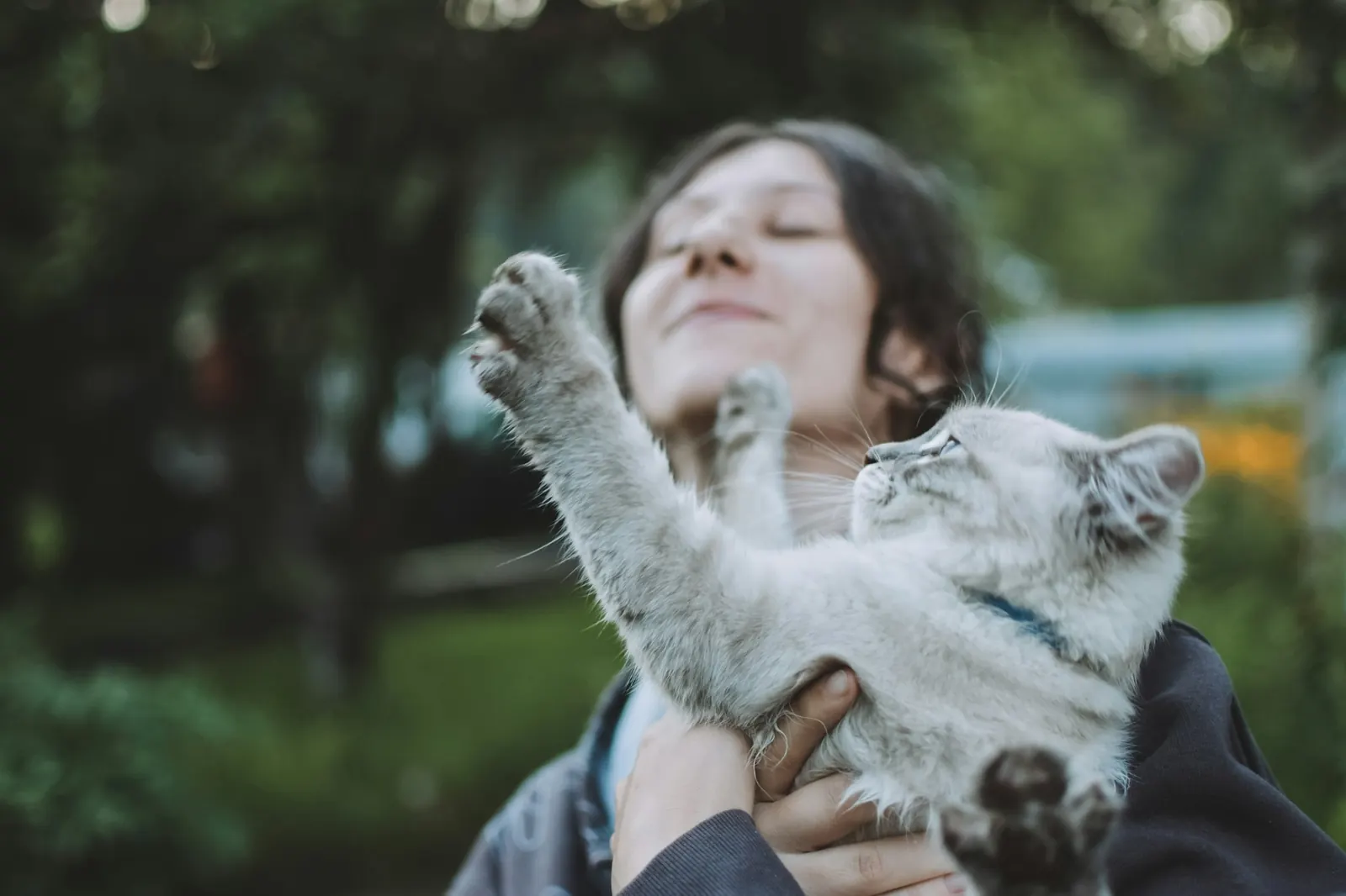 Smiling woman holding a playful white and grey cat outdoors