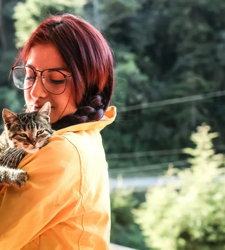 Woman in a yellow jacket holding her tabby cat on a porch