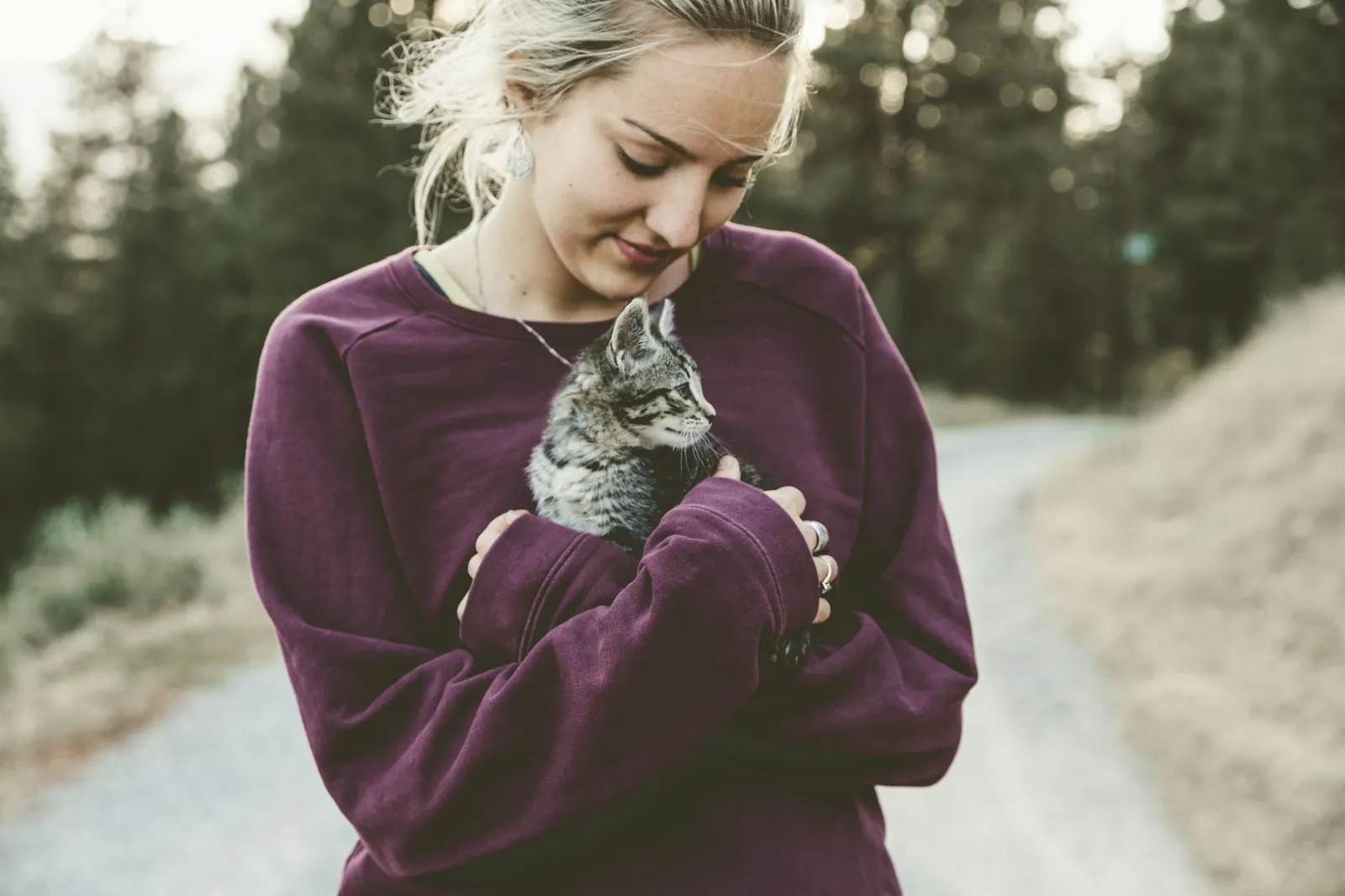 Woman gently hugging a grey tabby kitten on a country road