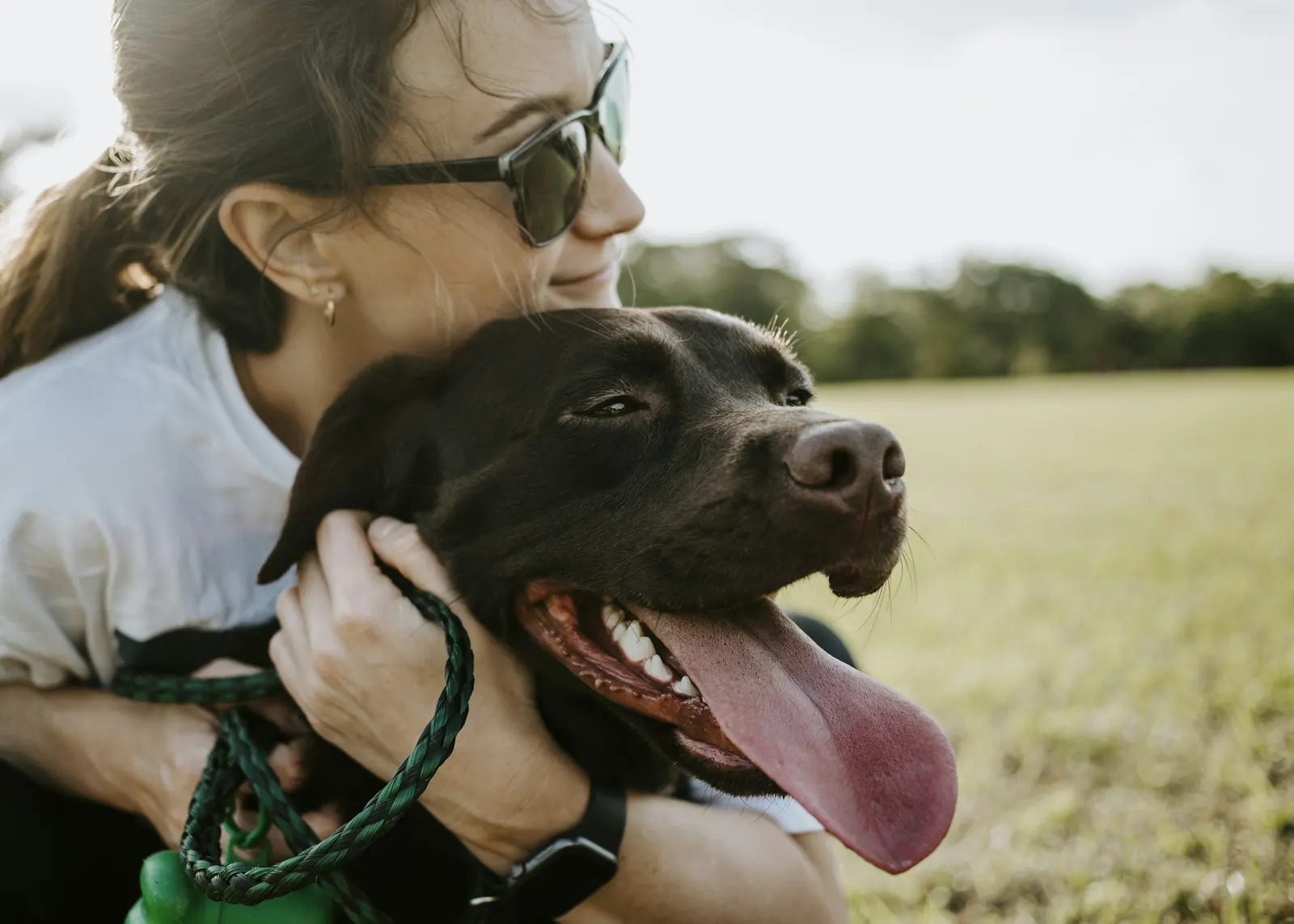 Smiling woman hugging a happy black dog in a grassy field