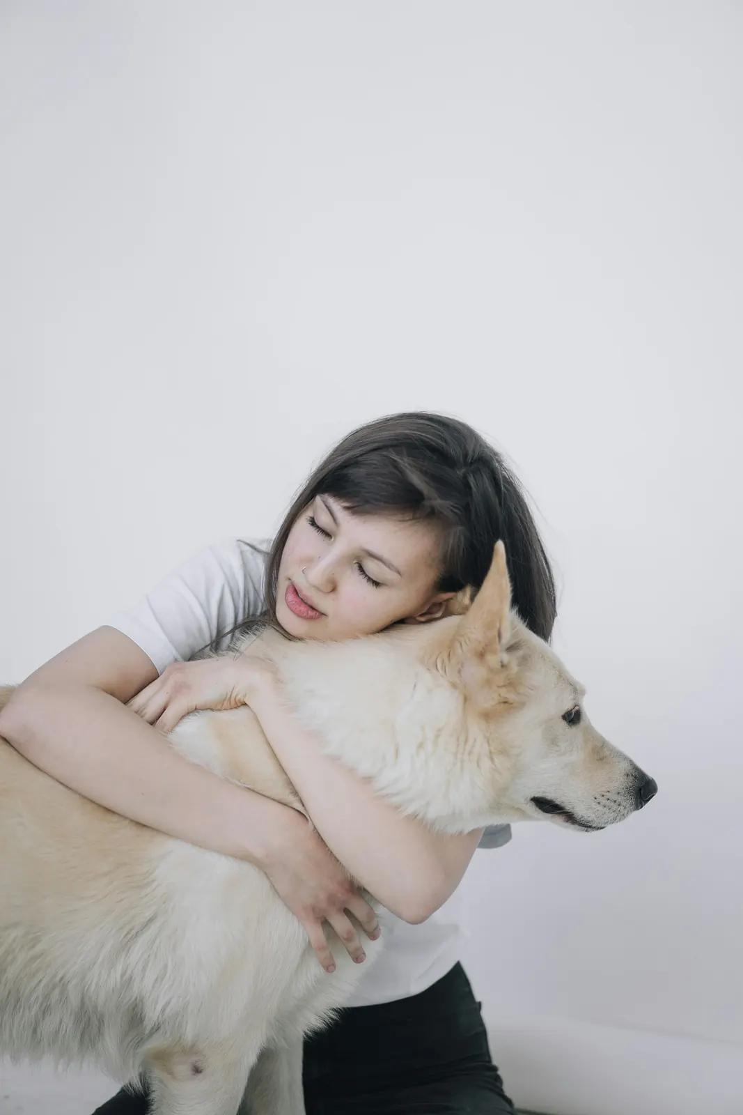 Young woman hugging a white fluffy dog against a pale wall