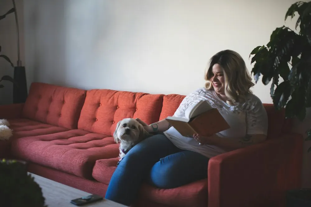 Woman reading on a red couch with her small dog