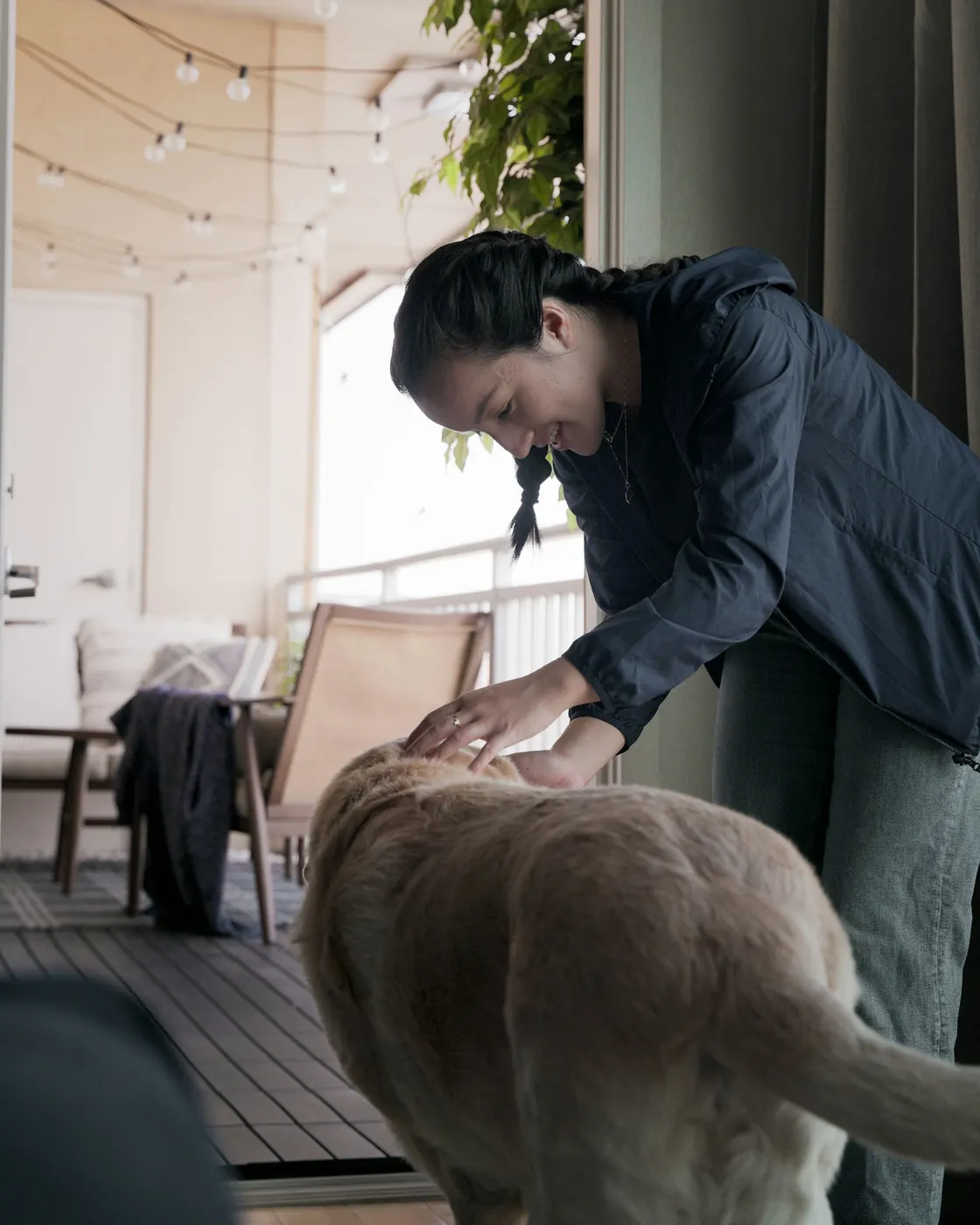 Woman bending down to warmly greet a golden dog on a sunny porch
